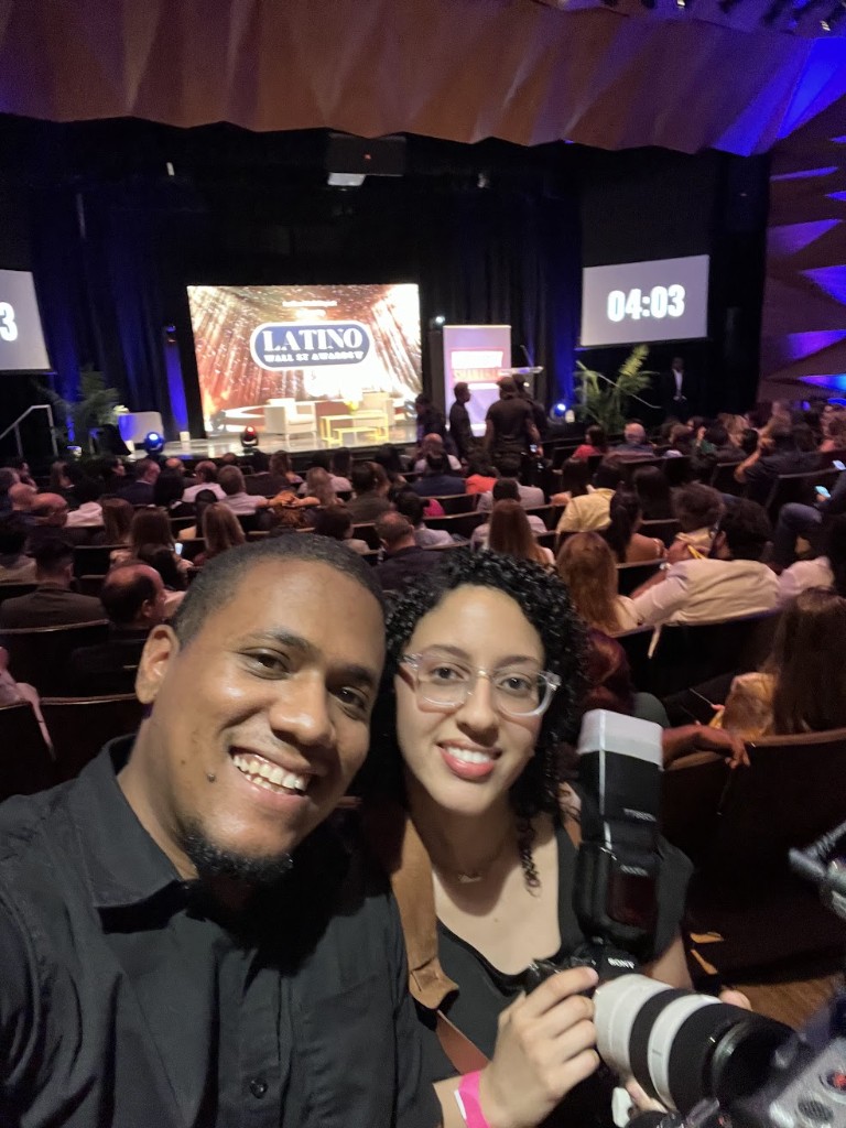 Solfilms crew selfie at Latino Wall Street Awards in a theater, Sony camera with telephoto lens, stage and audience in the background